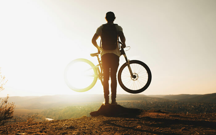 a man carrying a bicycle in the sunshine