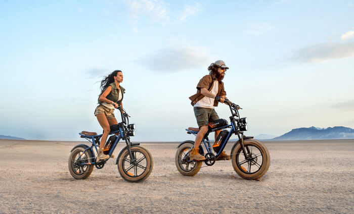 a man and a woman riding engwe m20 2.0 electric fat tire bikes on the sand