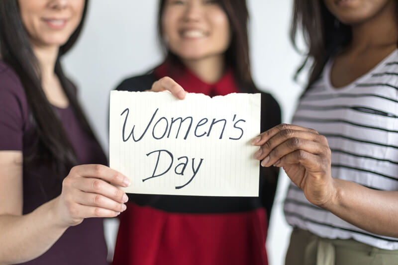 3 women holding a piece of paper with "women's day" written on it