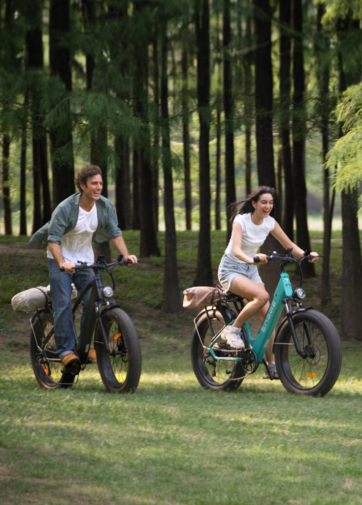 a man rides a galaxy grey e26 and a woman rides a gem blue e26 fat tire electric bikes on the grass