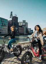 2 women ride a snow white and a flamingo pink engwe l20 fat tire electric bikes by the river