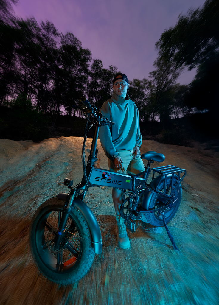 a man stands next to a black engwe engine pro e-bike on the sand